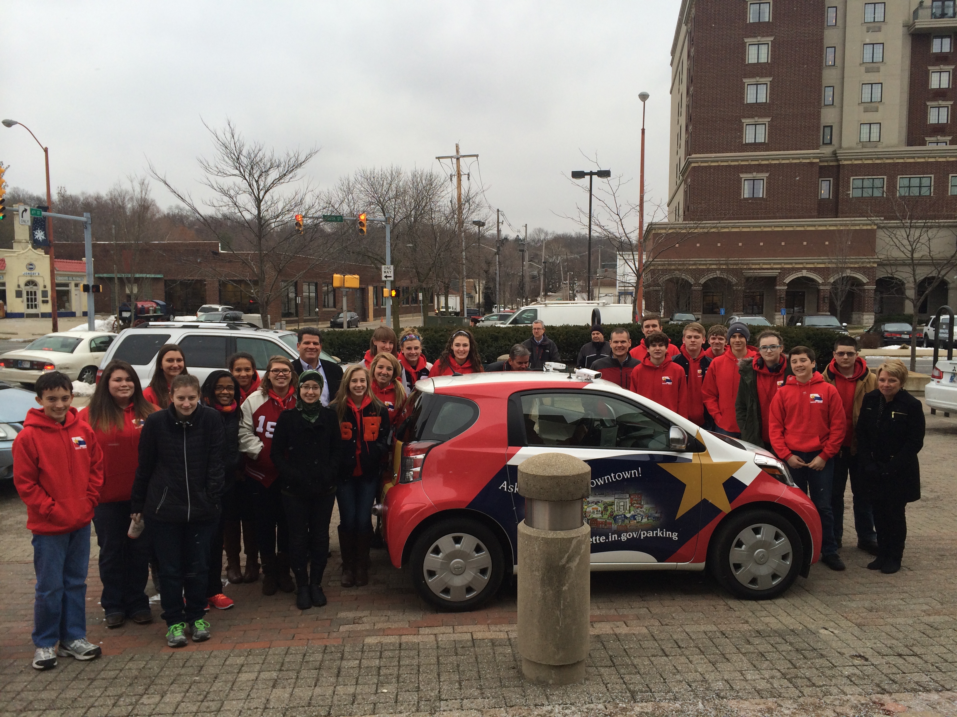 A group of teenagers standing next to a smart car